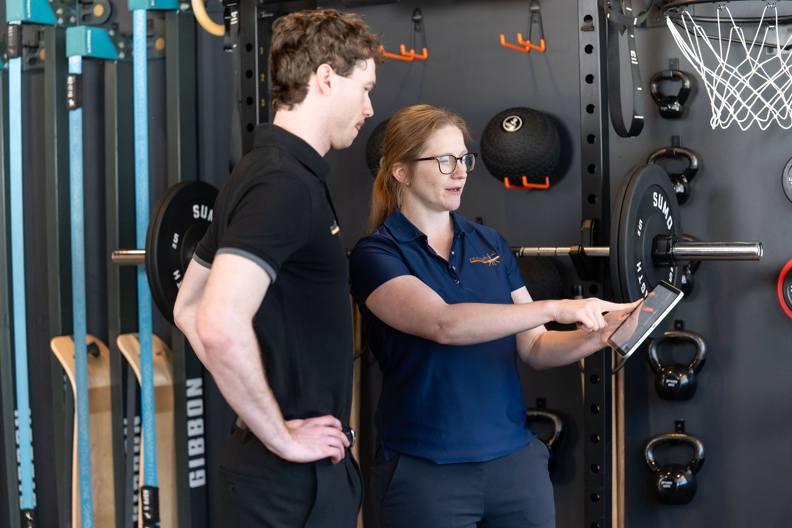 A physiotherapist showing a client data on a tablet while reviewing his exercise plan in the gym